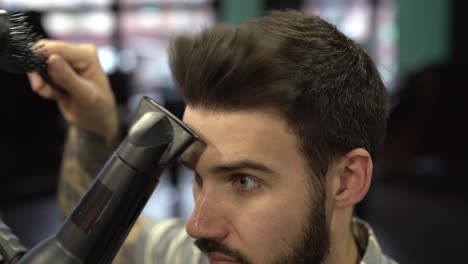 joven apuesto hombre barbudo se está peinando con peine y secador de pelo