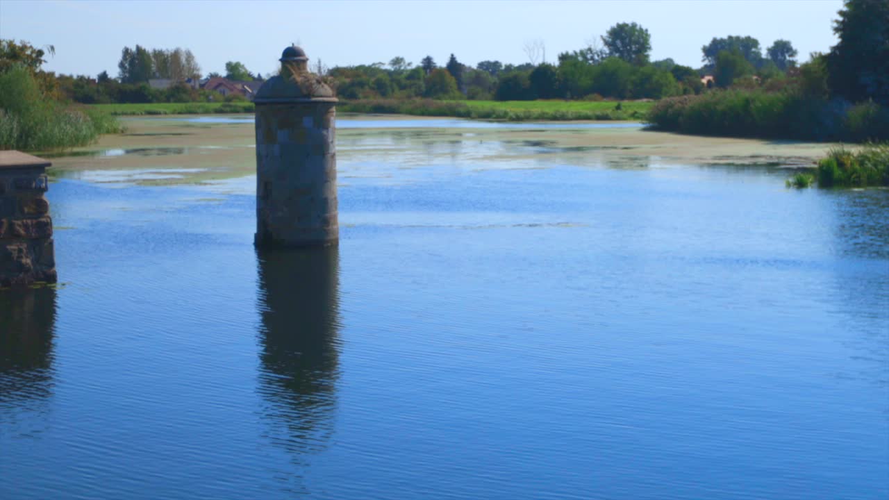 Static wide shot of mossy river in Gdansk with old tower inside during beautiful sunny day.