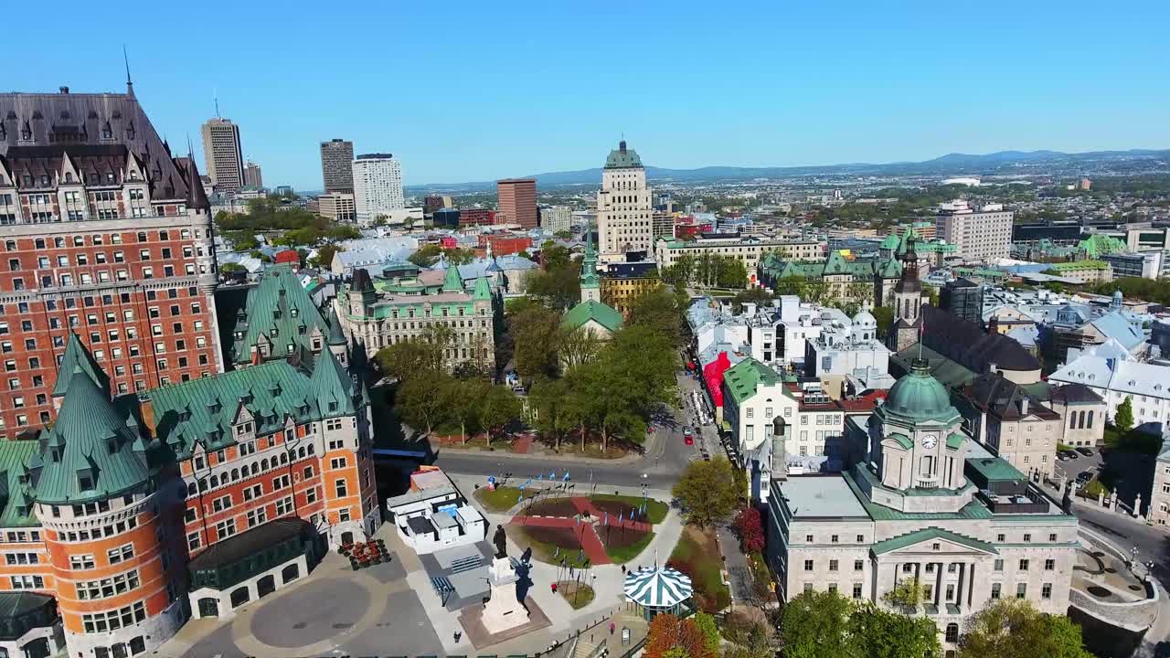 Chateau Frontenac rises above historic Old Quebec as cityscape overlooks wide Saint Lawrence River creating bright panoramic scene captured from smooth aerial drone view on clear day
