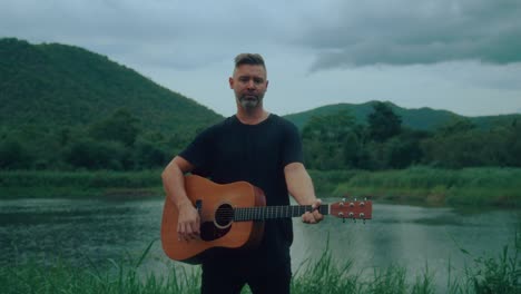 man playing acoustic guitar by a river