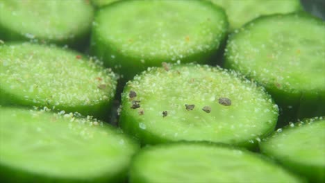 a macro close up shot, falling pepper grains on a cut slices of a fresh salted green cucumber, slow motion 4k video