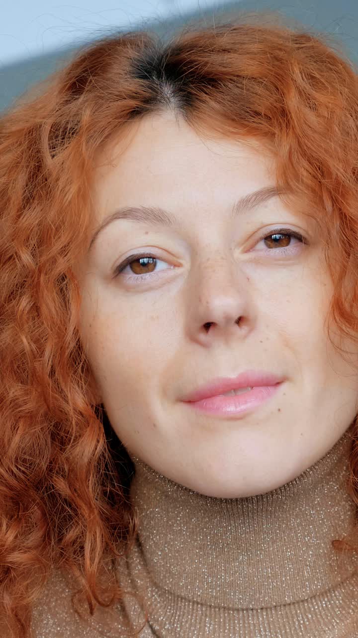 Woman with curly red hair is focused on laptop screen, showcasing concentration and engagement in a modern workspace environment with soft lighting