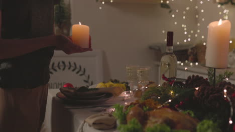mujer irreconocible poniendo una vela en la mesa de la cena de navidad en casa