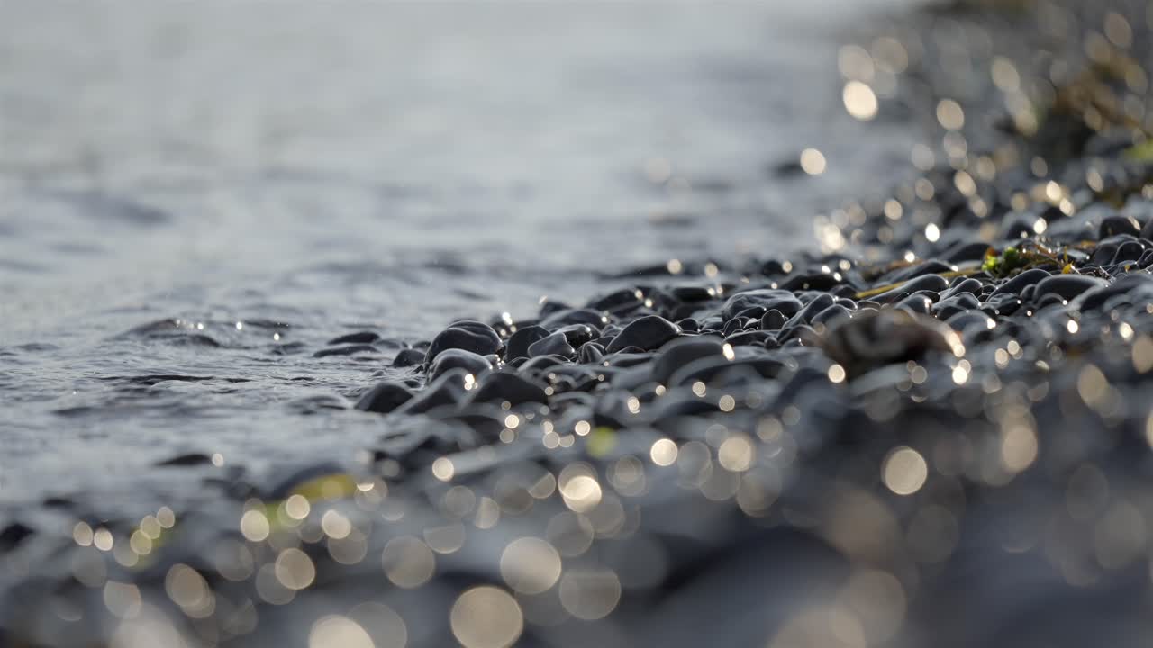 Close-up of a Gentle Wave Splashing on Wet Pebbles on a Rocky Beach