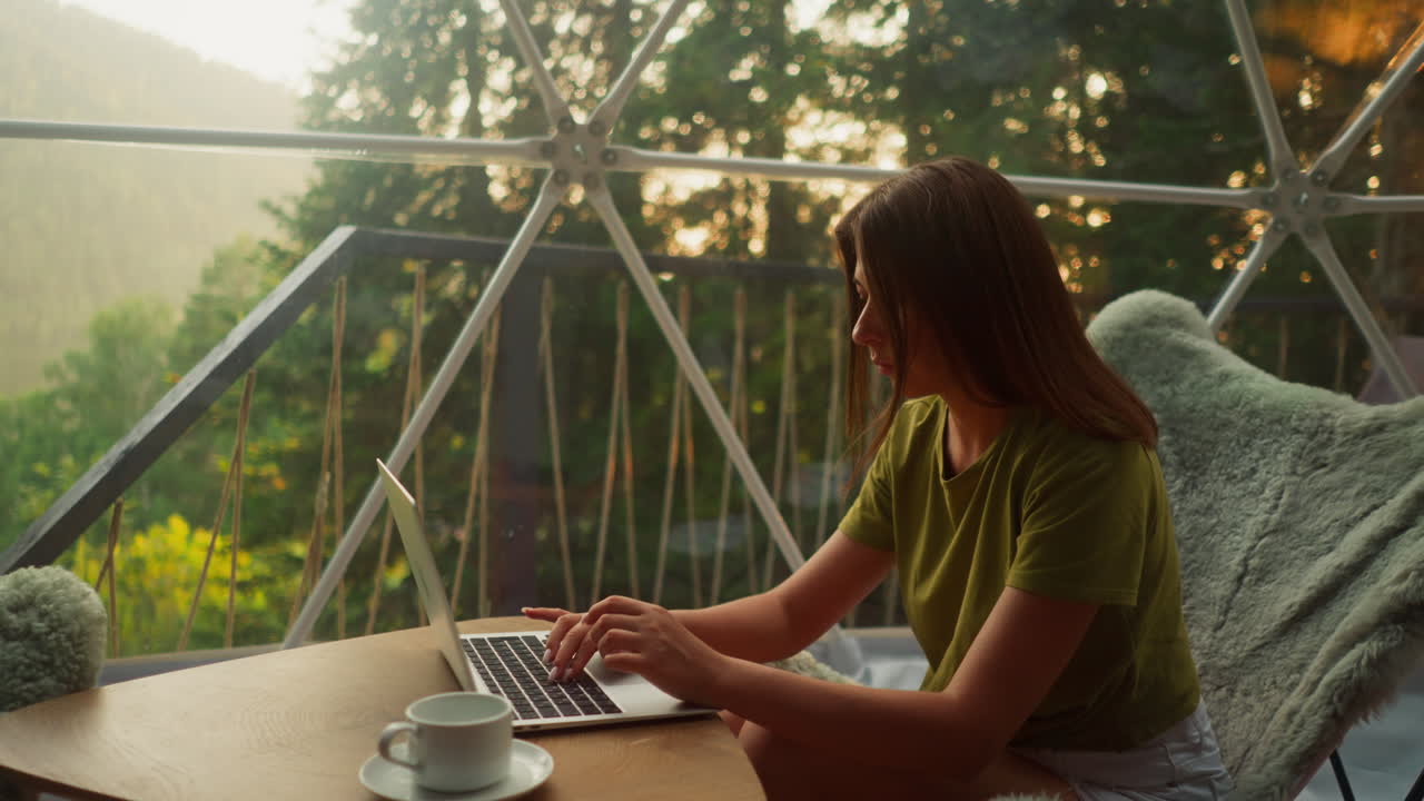 Concentrated lady works online on laptop drinking coffee in light premise with breathtaking view of nature beauty. Earnings and rest slow motion