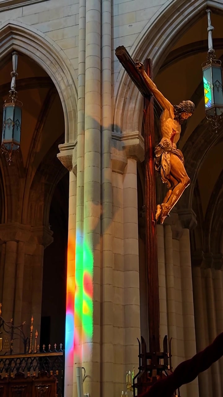 8 agosto 2025, Madrid, Spagna: Crocifisso in legno con riflesso di luce arcobaleno su un pilastro della cattedrale