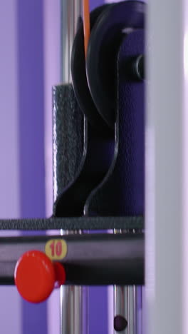 toma de primer plano de la pila de pesas que desciende en el equipo de gimnasio con barras metálicas y un fondo púrpura vibrante, centrarse en el movimiento y el entrenamiento de resistencia a medida que el peso se mueve hacia abajo