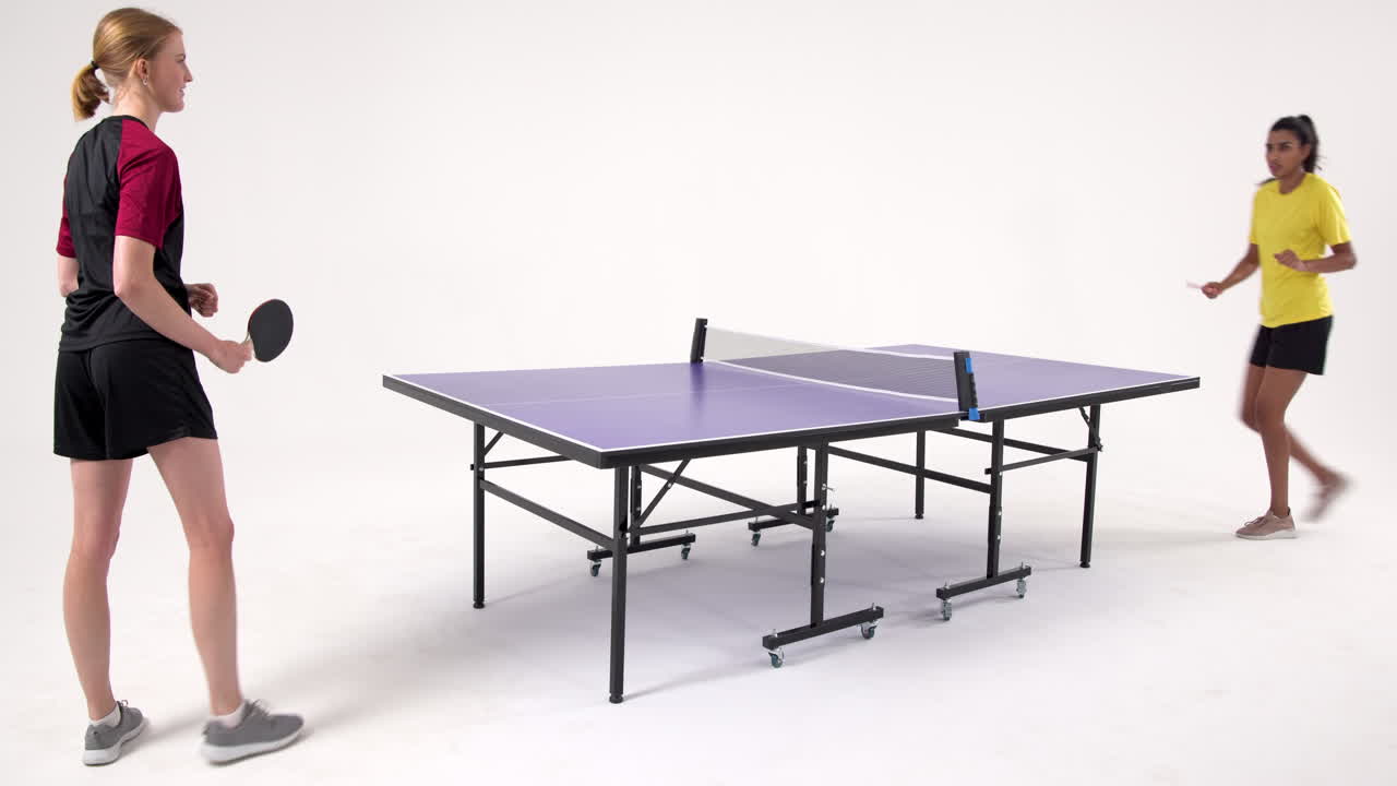 Playing table tennis, two women competing intensely in studio setting