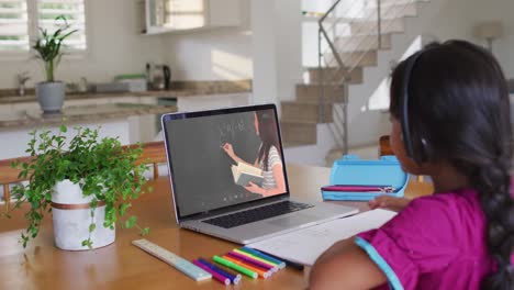 chica afroamericana haciendo la tarea mientras tiene una videollamada con una maestra en una computadora portátil en casa