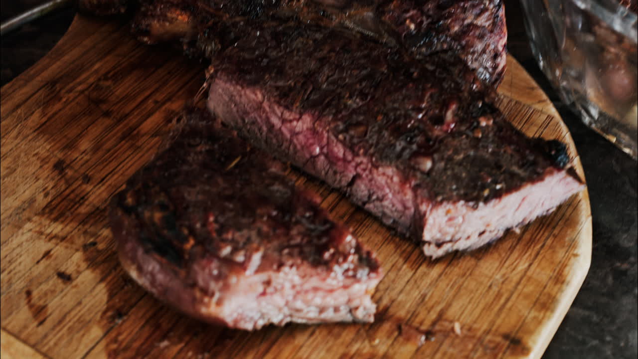 Close-up of a man's hand carving a grilled steak on a rustic wooden cutting board