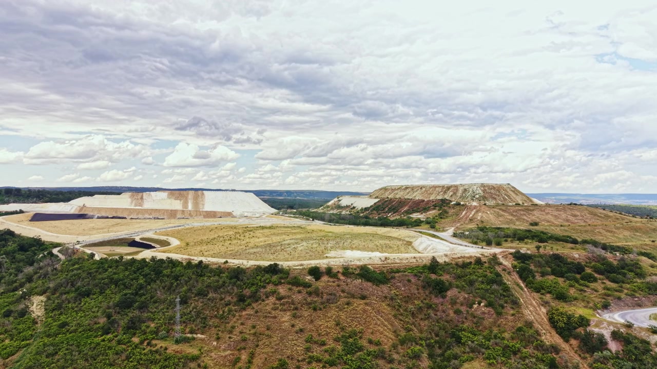 Vista de um local de mineração com grandes formações de terra e céu nublado perto de uma área rural durante o dia
