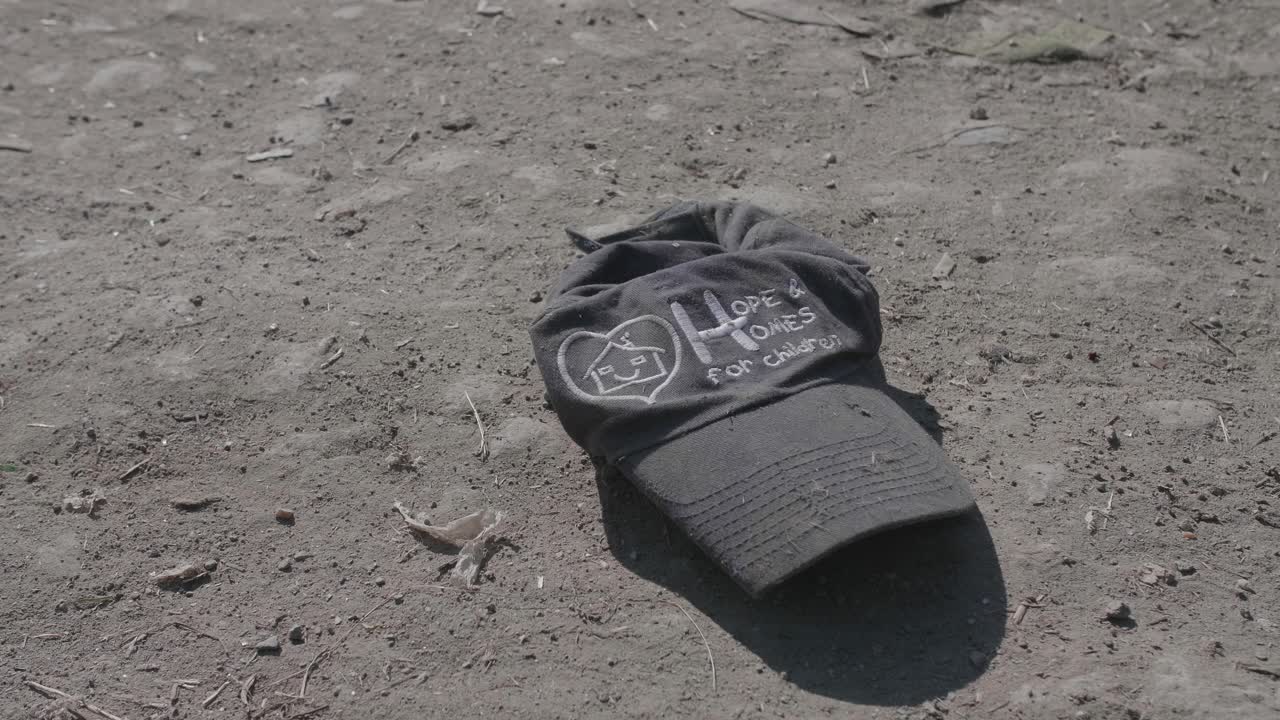 A dirty cap from the 'Hope and Homes for Children' charity lies discarded on the ground, a poignant and ironic symbol of lost hope, childhood poverty, and social crisis.