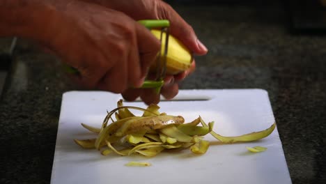 hombre de piel marrón de mediana edad pelando patatas con un pelador en una tabla de cortar blanca en casa 2