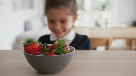 mischievous girl wearing school uniform taking strawberry from kitchen counter