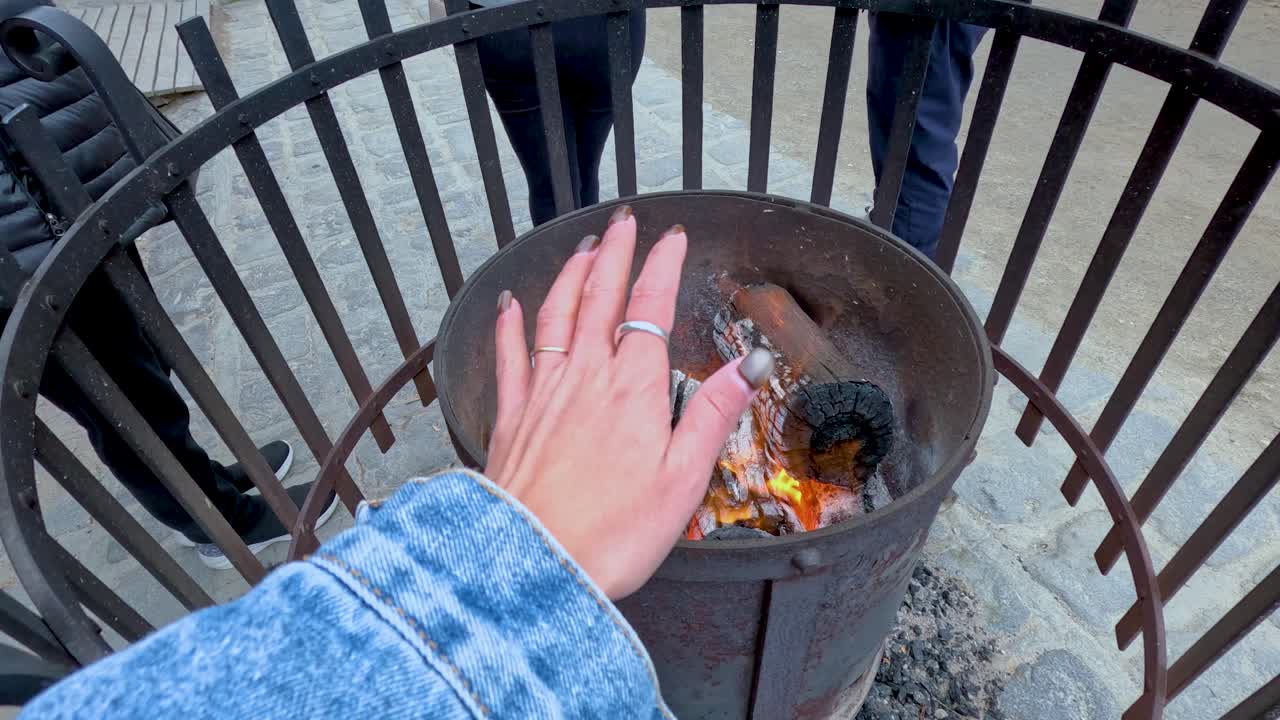 A person warms their hands over a small bonfire, capturing a cozy moment in an outdoor setting