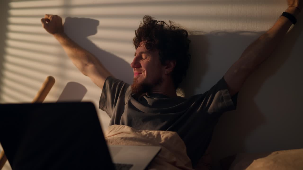 hombre estirándose en la cama con una computadora portátil