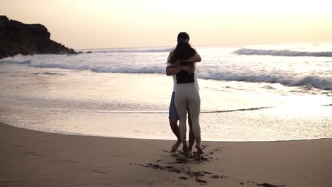 Young-beautiful-couple-walking-by-the-sea.-Boy-and-girl.-They-are-happy.-Tall-guy-takes-the-tiny-girl-in-his-arms-and-turns-her-around.-Silhouettes-on-an-ocean-background