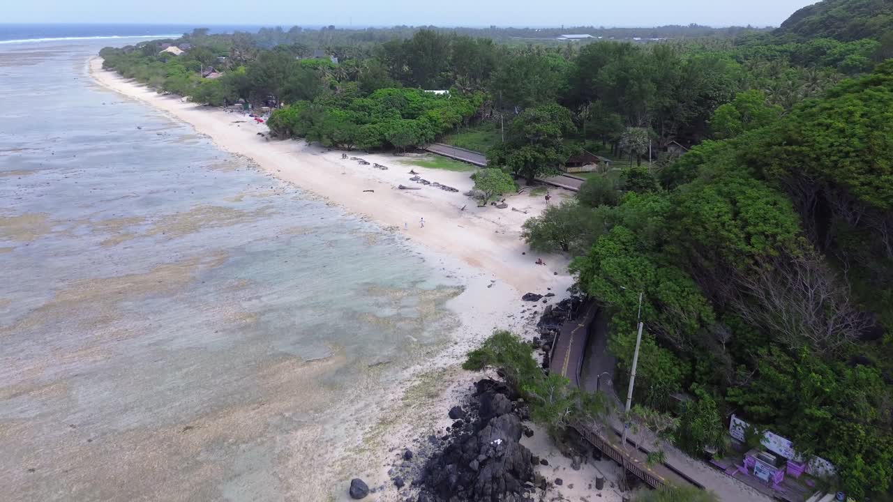 Aerial pulls back over the coast revealing the sand, rocks and dense greenery