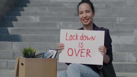 woman holding sign saying 'lockdown is over' on stairs