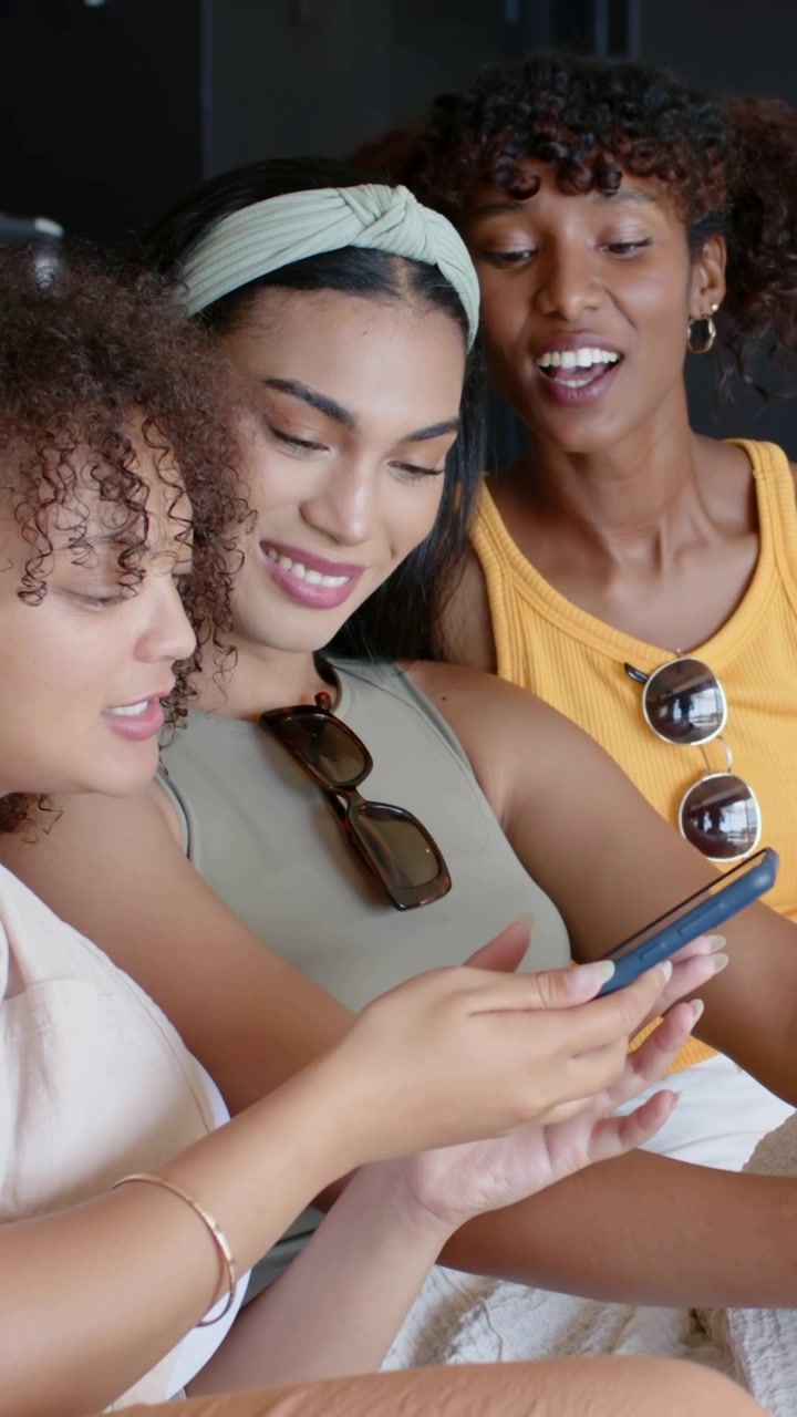 Extending blue phone, three women taking selfie, reviewing photos in lounge, middle woman pointing