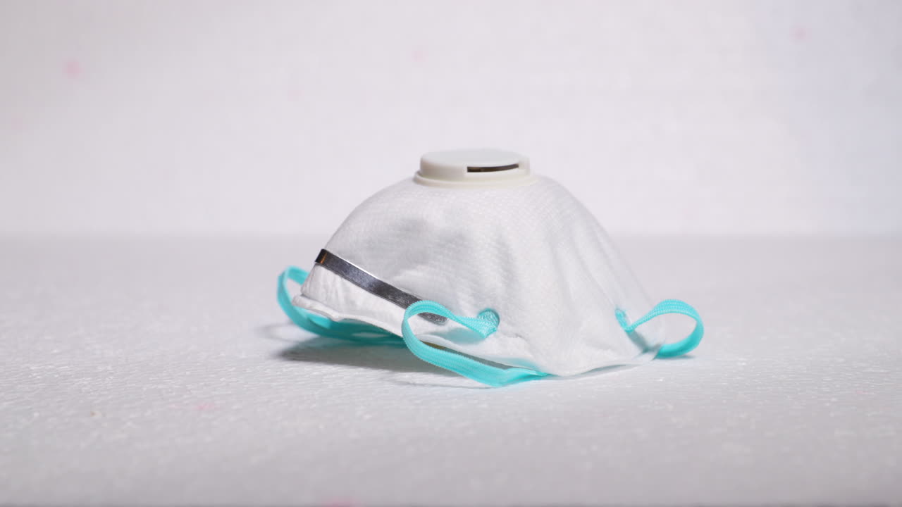 Hand lifting protective facial white mask mask FFP2 from threat like corona covid-19 virus on white backing that protects mouth and nose on plate capture in 4k 60fps