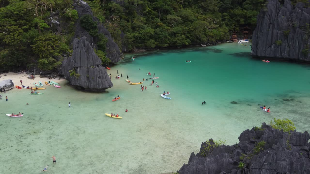 Turistas practicando kayak y nadando en la tropical Laguna Cadlao de color esmeralda, El Nido, formaciones rocosas kársticas en la isla, Filipinas, vista aérea