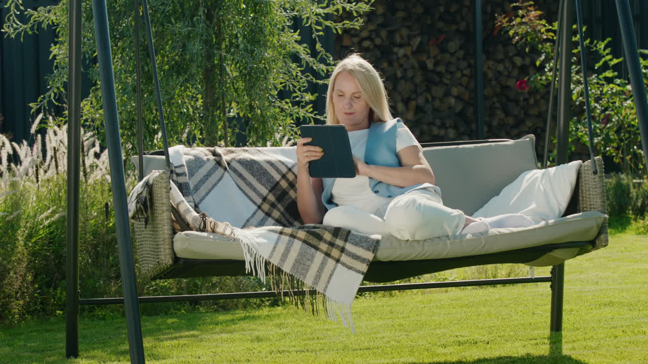 Sød kvinde bruger en tablet. Hviler i en havesofa i husets baghave