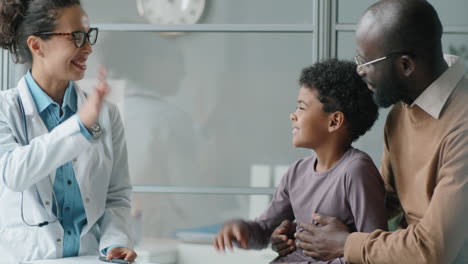 little african american boy speaking and giving high five to female pediatrician