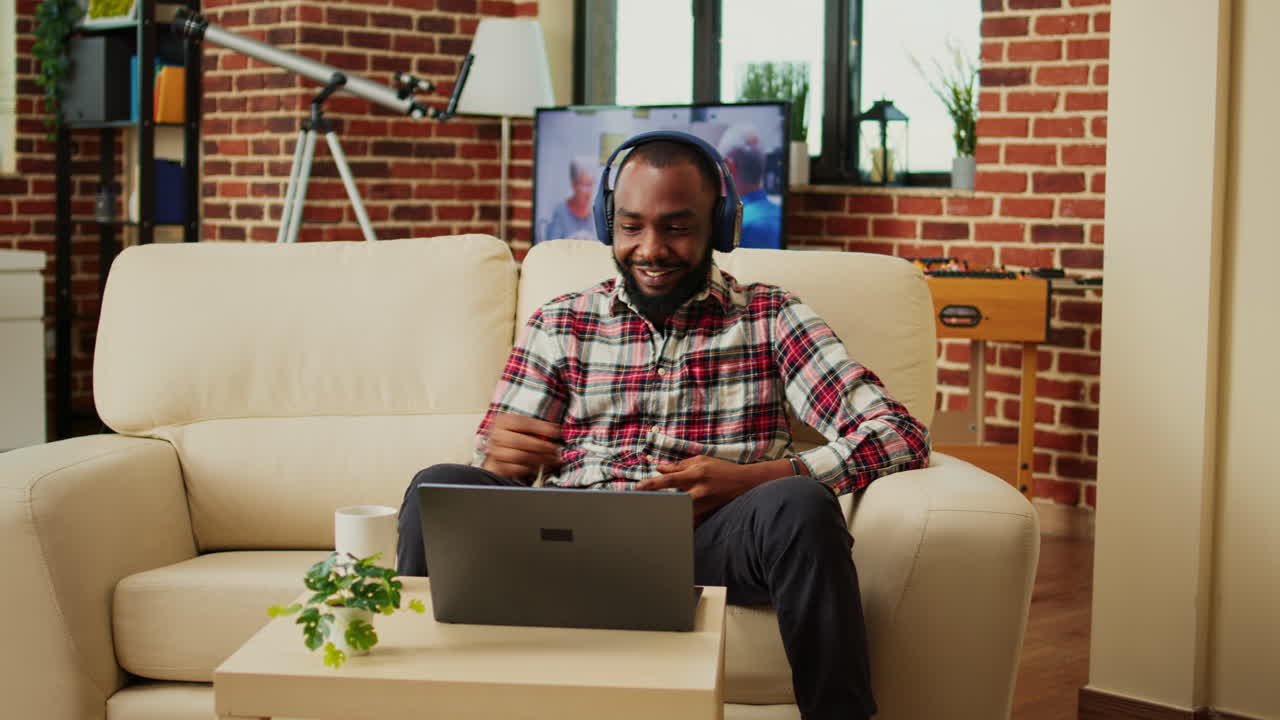 Man on couch using laptop with headphones for a video call