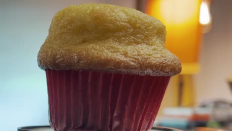 un primer plano de un muffin dorado en un envoltorio rojo con una lámpara borrosa en el fondo
