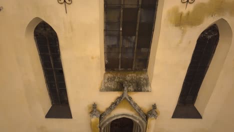 un pedestal acercándose a un dron que captura la entrada y una gran ventana encima de ella, de una iglesia arquitectónica antigua en la ciudad de sighisoara en una tarde