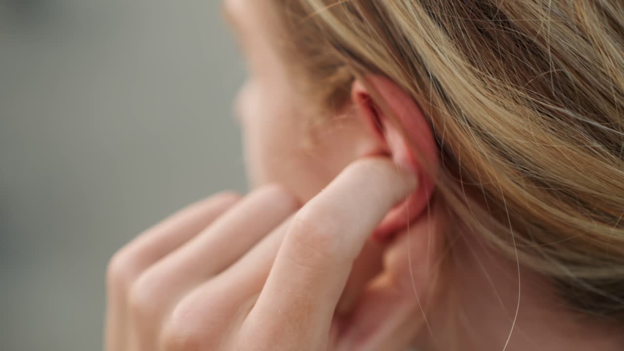 Donna sul palco regola il monitor con il dito concentrato durante le prove dietro le quinte, capelli biondi raccolti dietro l'orecchio, si prepara per il concerto, controllo audio e tempi, preparazione concentrata per la performance.