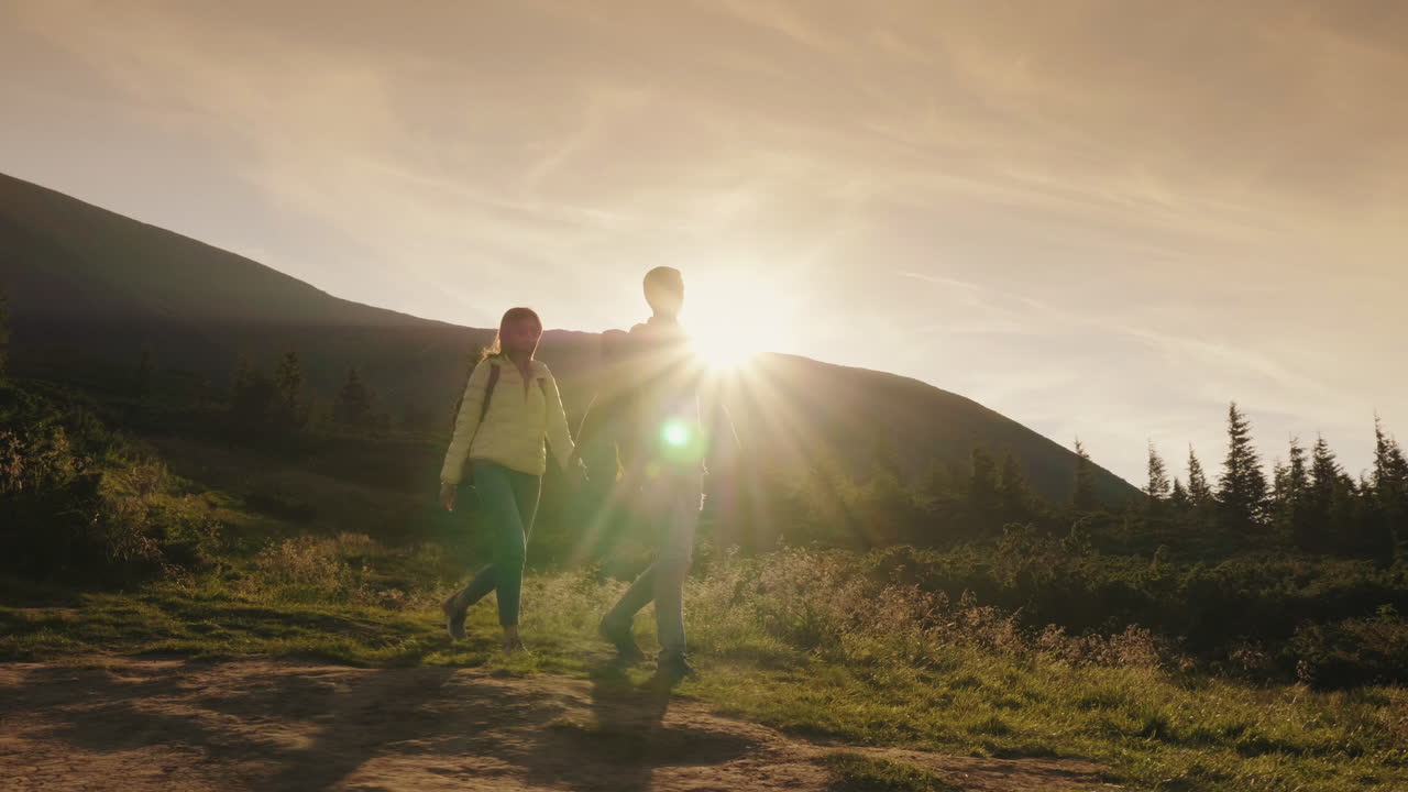 joven pareja de turistas tomados de la mano caminando por un sendero de montaña en los rayos del sol poniente
