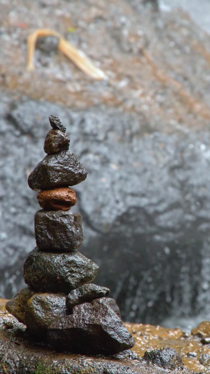 A vertical stack of balanced stones stands before a blurred waterfall in Ngardmau, Palau