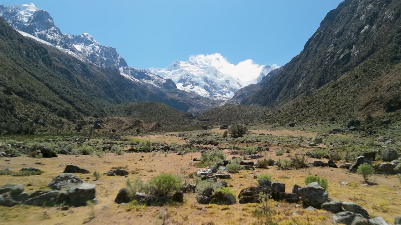 Majestic low aerial shot of the Cordillera Blanca in Peru’s Andes showing towering snow-capped peaks, dramatic green valleys, and glacial landscapes under a clear blue sky