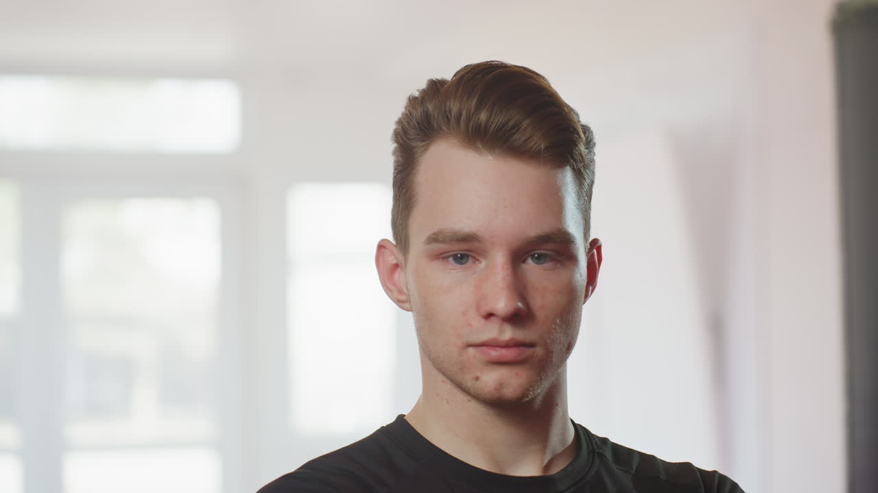 Man in black long sleeve shirt crosses arms inside gym with serious focused expression, showing confidence, discipline, strength, determination, and resilience while preparing for workout session