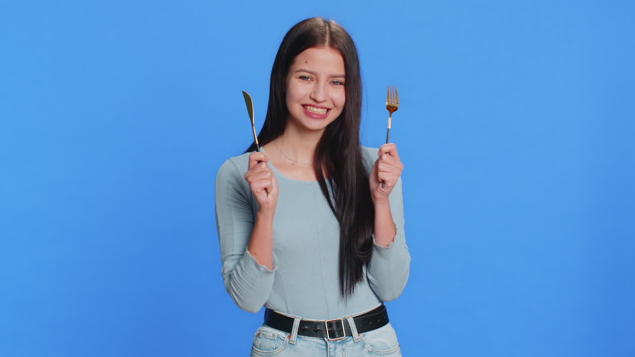 ⁇ 주린 여자가 저녁 식사 식사 접시를 위해 기다리고 불안으로 식구 포크 칼을 들고 있습니다.