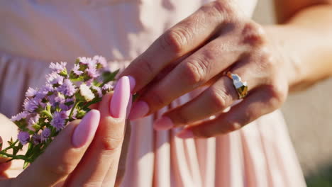 close-up of woman's hands with pink manicure holding purple flowers