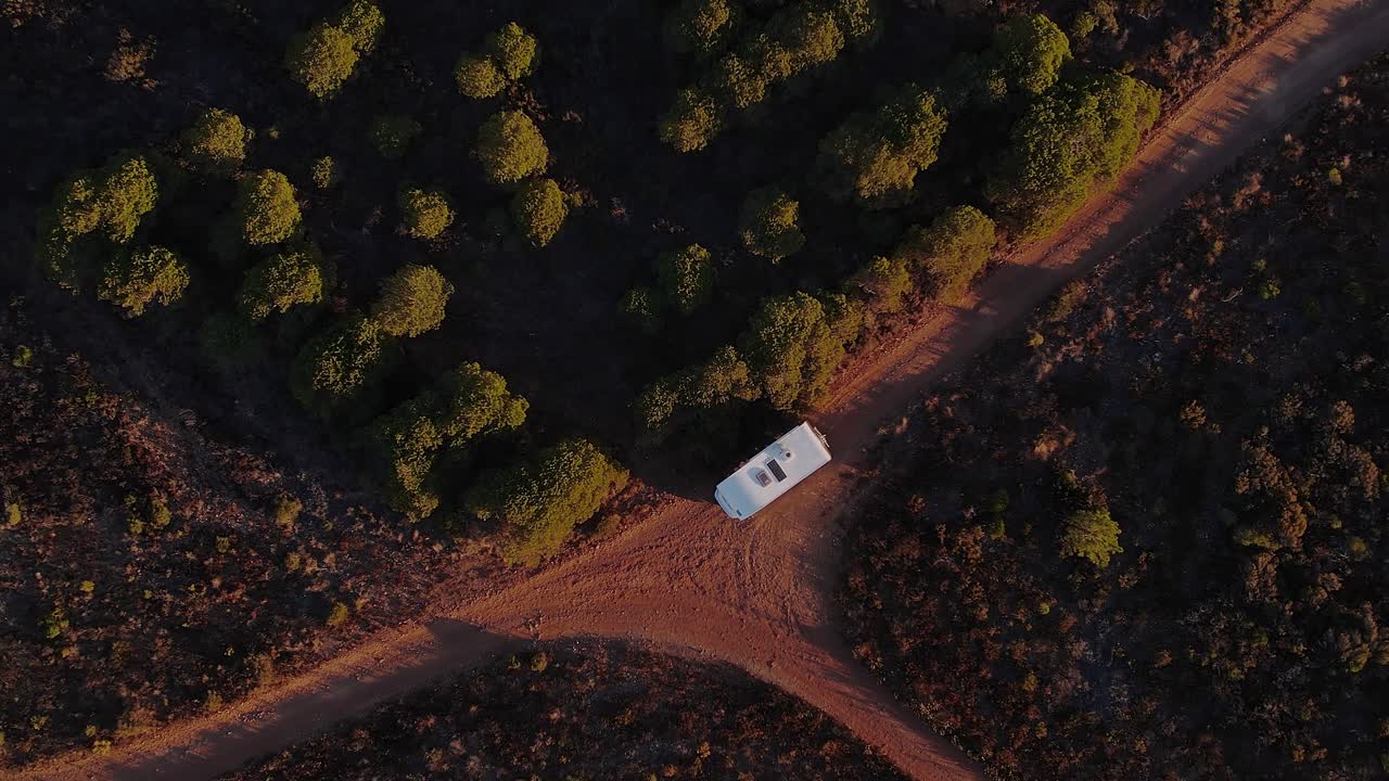 Portekiz, Almada, Costa da Caparica'daki Arriba Fóssil'in kumlu platosunda, Akdeniz çalılıkları ve sıcak gün batımı ışığıyla çevrili karavan sürüşü, drone dikey olarak yukarıdan aşağıya doğru yükseliyor.