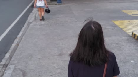 overhead following shot of young asian female uncomfortably walking along city sidewalk