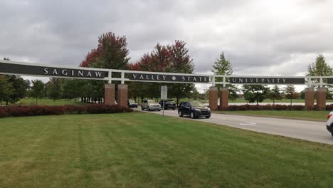 Entrance-with-cars-driving-on-the-campus-of-Saginaw-Valley-State-University-in-University-Center,-Michigan-in-slow-motion-wide-shot