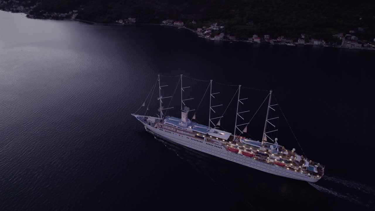 Kotor, Karadağ'daki Kotor Körfezi'nde gün doğumunda seyreden MSY Wind Surf kruvaziyer gemisinin havadan görünümü, büyüleyici gün doğumu ışığı, sakin atmosfer ve doğal güzelliği vurgulayan yüksek kaliteli drone çekimi.