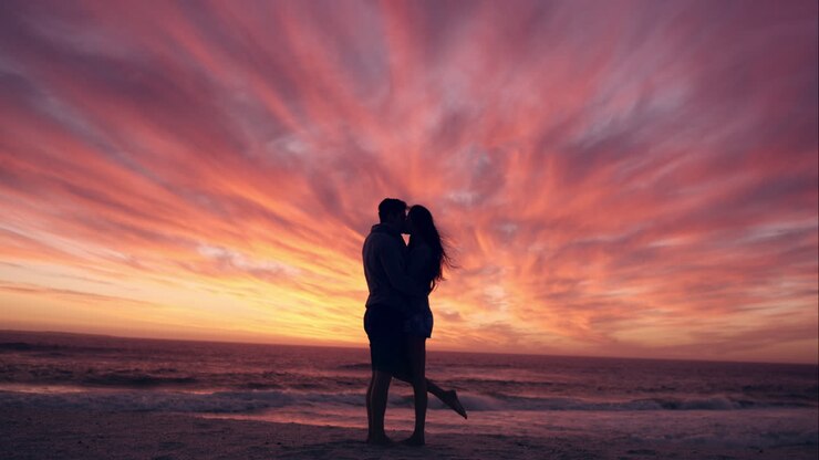 Coppia felice che si bacia in spiaggia al tramonto, silhouette di innamorati in luna di miele RED DRAGON