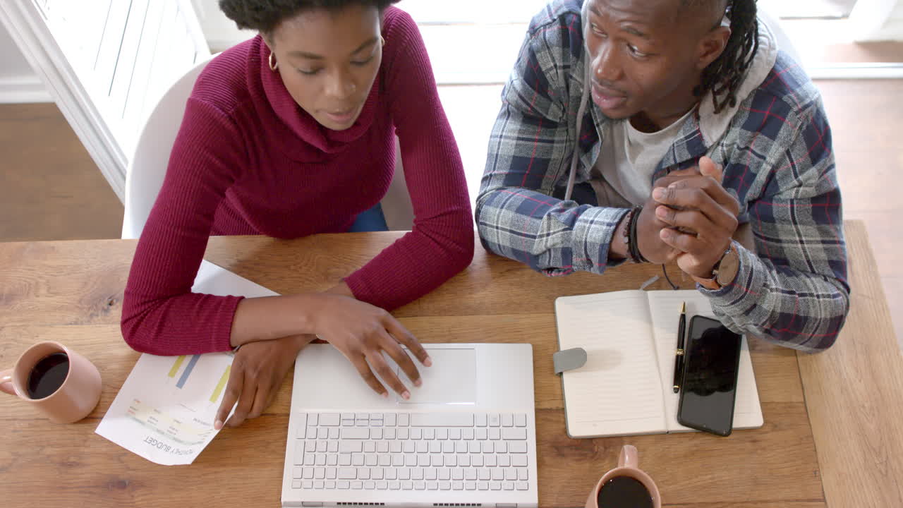 Working together, African american couple using laptop and discussing documents at home office