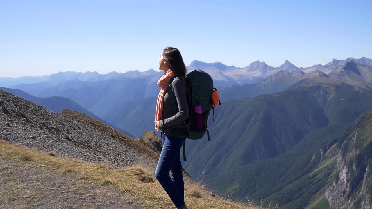 Donna escursionista su un crinale montano con sciarpa arancione e un grande zaino, che ammira le vaste vette alpine.