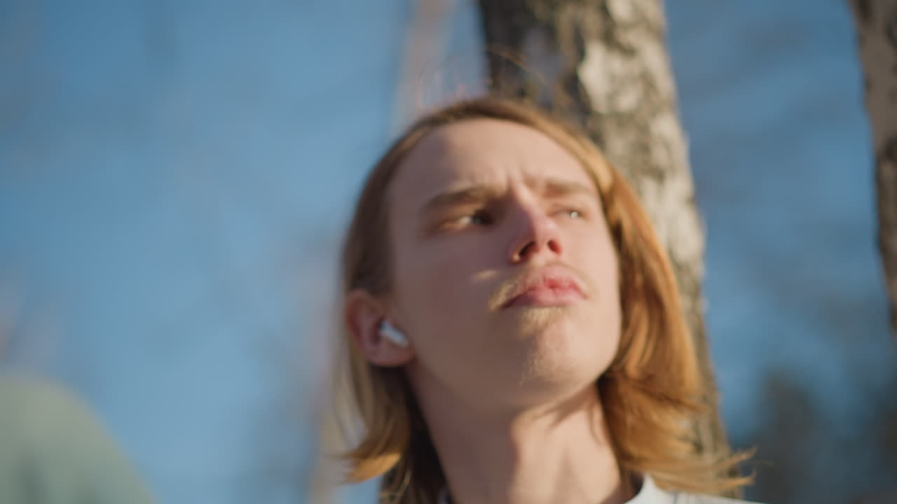 Молодые люди размышляют на открытом воздухе, юноша задумчиво стоит среди тихих деревьев, подросток созерцательно стоит под мягким солнечным светом в парке, юноша задумчиво смотрит на небо в тени берез