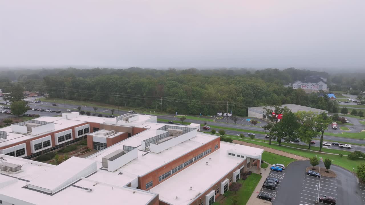 Rising drone shot of american school with flag and parking yellow school bus. Grey sky in autumn season. Suburb district of American town. Wide shot panorama.