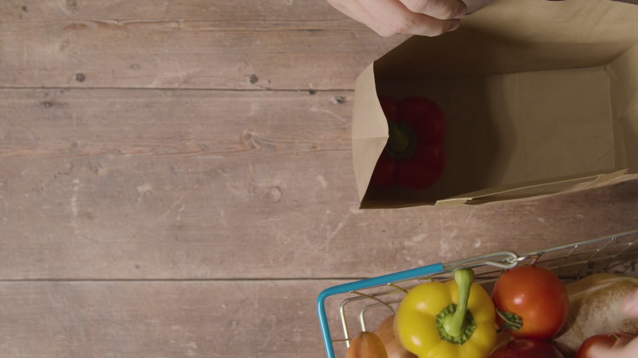 슈퍼마켓 와이어 쇼핑 바구니에서 종이 봉투에 기본 신선 식품을 포장하는 사람의 오버 헤드 샷