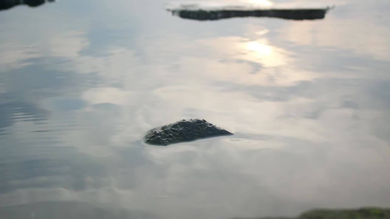 a rock over the calm lake water in the afternoon
