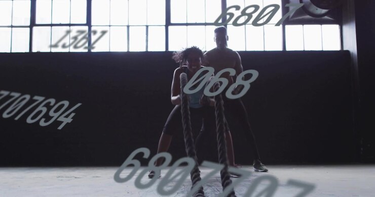 Woman Exercising with Battle Ropes in Gym with Personal Trainer